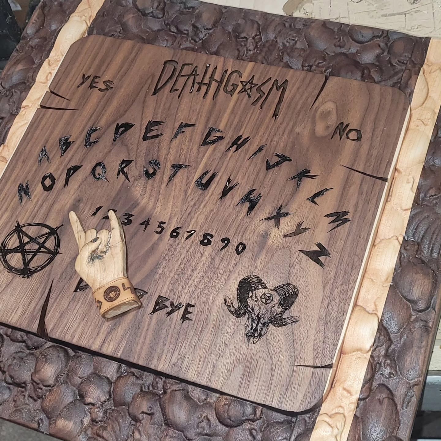 Carved wooden movie prop spirit board with lettering, skull relief border and hand-shaped planchette